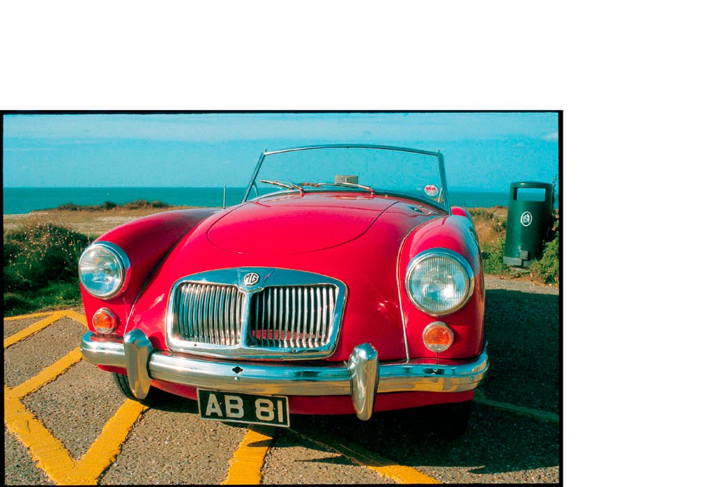 red MG parked at the beach with blue sky background